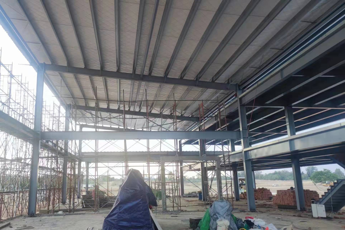 Interior view of the Emerald E-Commerce Center under construction in Naypyidaw, Myanmar, showcasing the vast H beam steel structure, floor decking sheet, and scaffolding for super structure work.