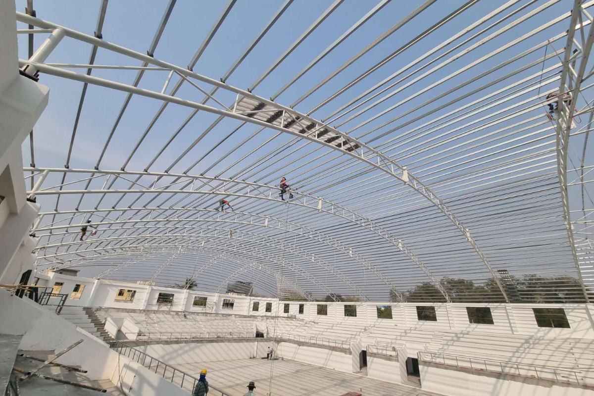 Detailed view of workers on the complex steel roof framing during the installation phase at Ba Htoo Indoor Sport Stadium in Mandalay, Myanmar.