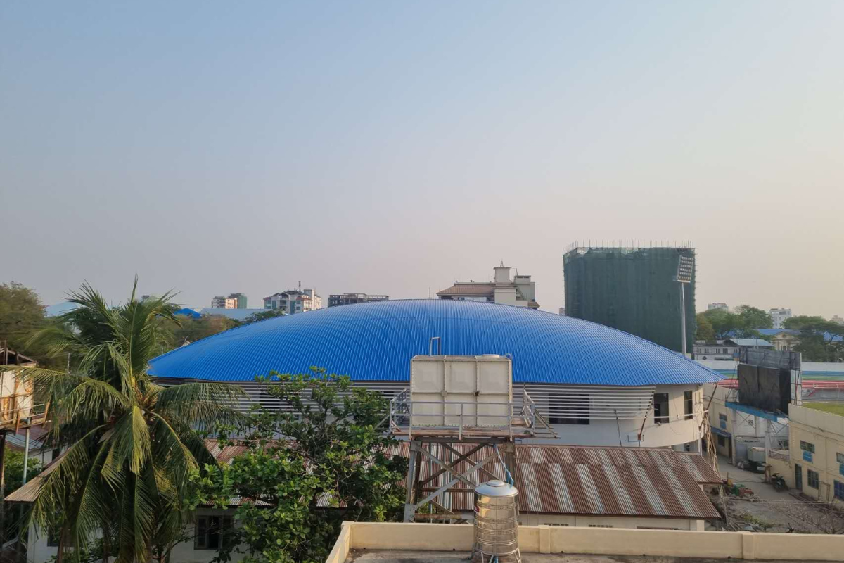 Exterior view of the completed Ba Htoo Indoor Sport Stadium in Mandalay, Myanmar, prominently featuring its distinctive blue arched roof.