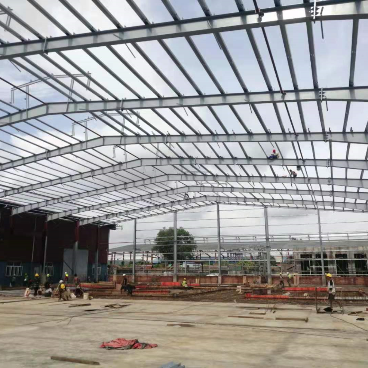 Steel frame erection in progress for a large warehouse at a Myanmar Yi Jin project site, with workers assembling the structural roof system and main framework.