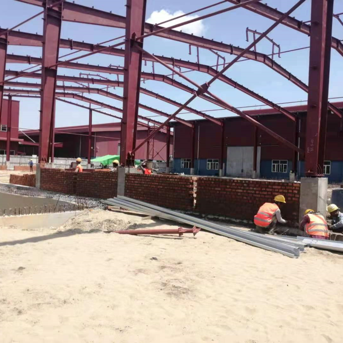 Brick wall construction in progress between the red oxide-primed steel frame of a warehouse at a Myanmar Yi Jin customer site in Myanmar, combining masonry techniques with the structural steel framework.