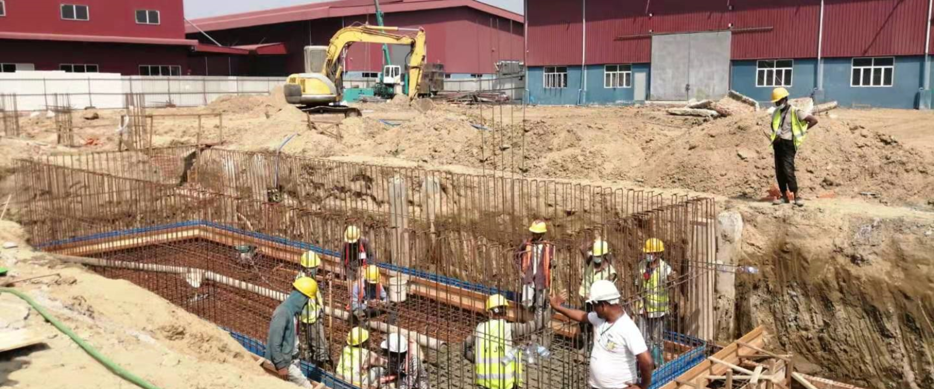 Workers constructing a reinforced concrete warehouse foundation with steel rebar installation at an industrial site in Myanmar, demonstrating the foundation stage of steel structure building.
