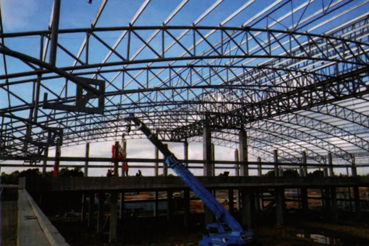 A large orange crane lifts a steel pipe truss section into place for the Europe & Asia Commercial (EAC) warehouse project in Mandalay, Myanmar.
