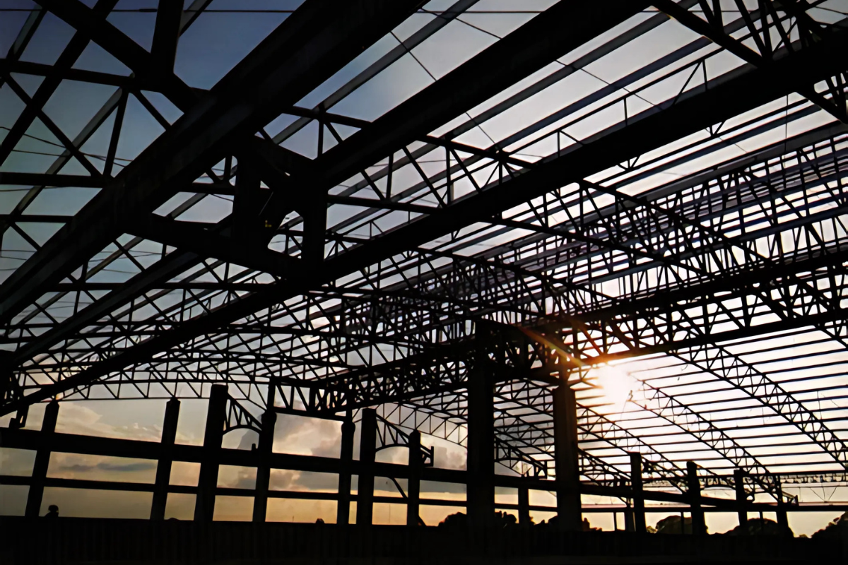 An interior view of the 60,000m² EAC Commercial steel structure warehouse in Mandalay, Myanmar, showing the intricate steel truss roof and a crane during the erection process.