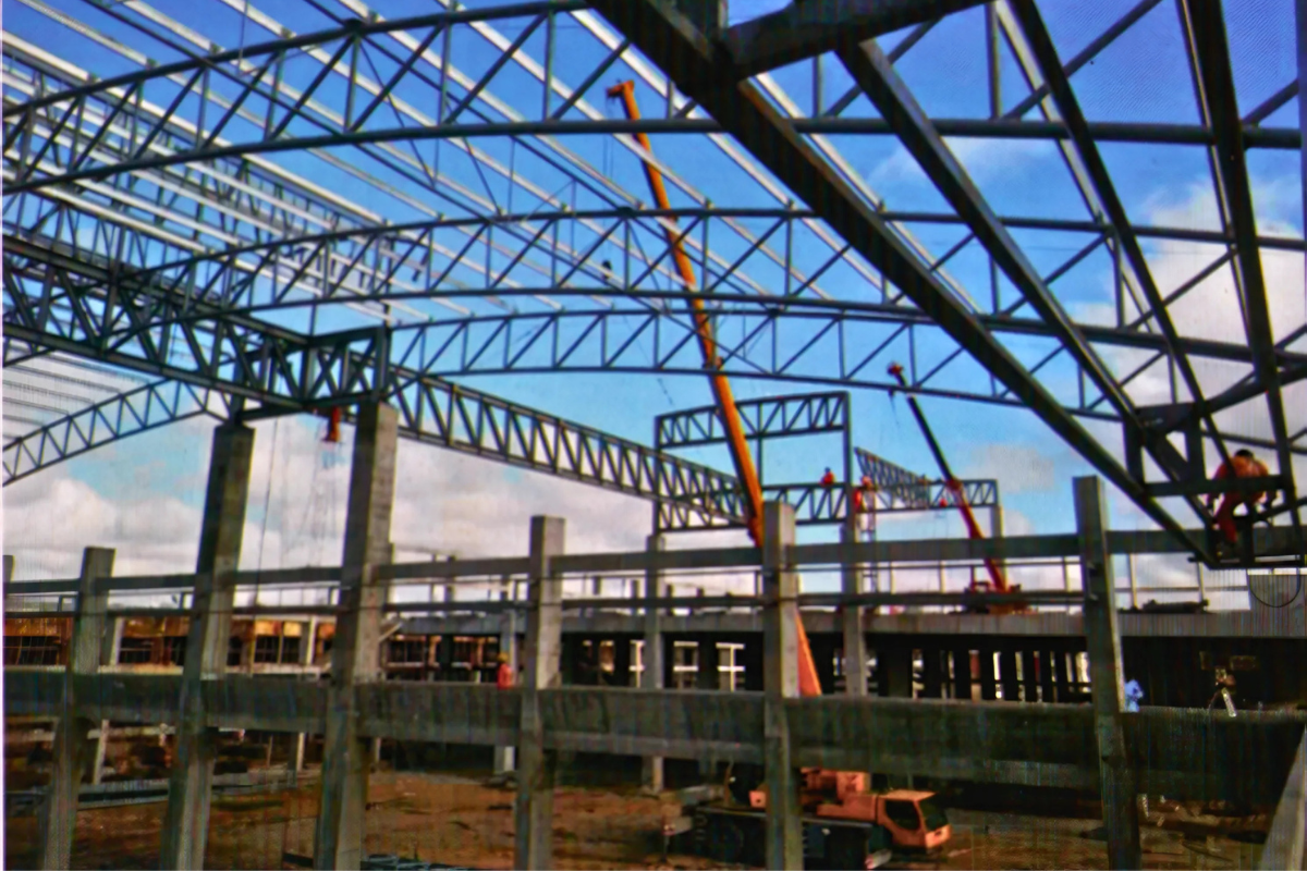The arc-shaped steel pipe truss roof structure being installed for the Europe & Asia Commercial (EAC) warehouse in Mandalay, Myanmar, with a blue crane and workers visible.