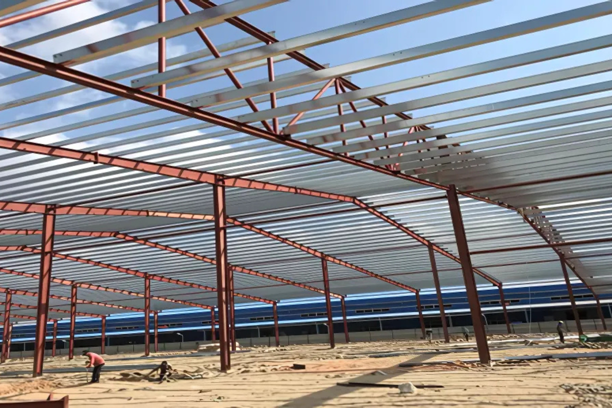 : An interior photo of the Myanmar Knitting Factory in Pathein, showing the steel structure frame and the installation of the corrugated metal roof sheets.