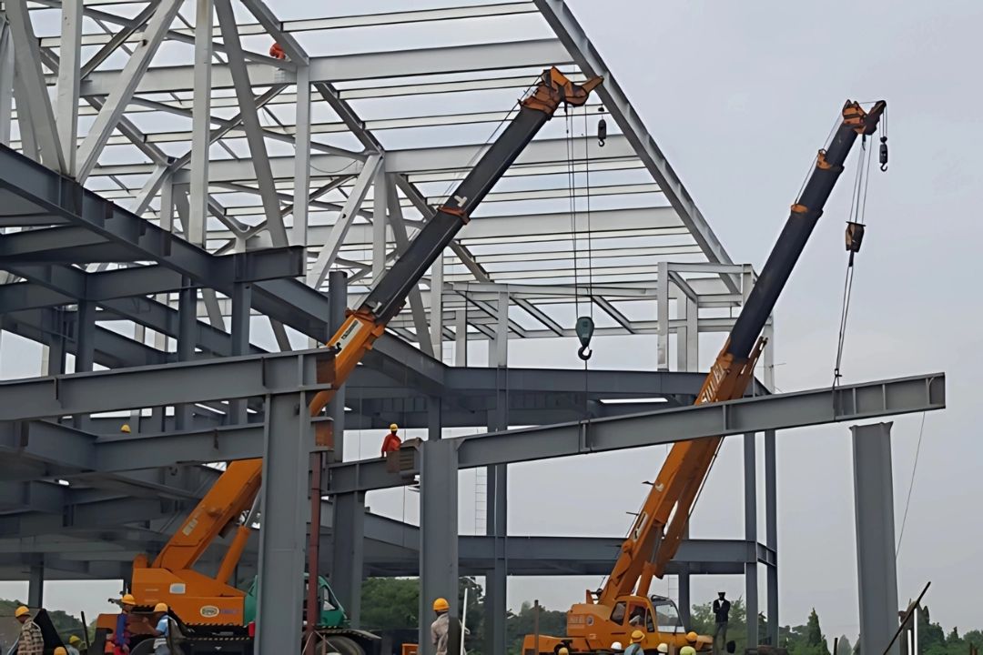 A construction site photo showing the ongoing steel structure installation for the Mandalay Convention Center, a project by Myanmar Yi Jin, with a crane operating in the background.