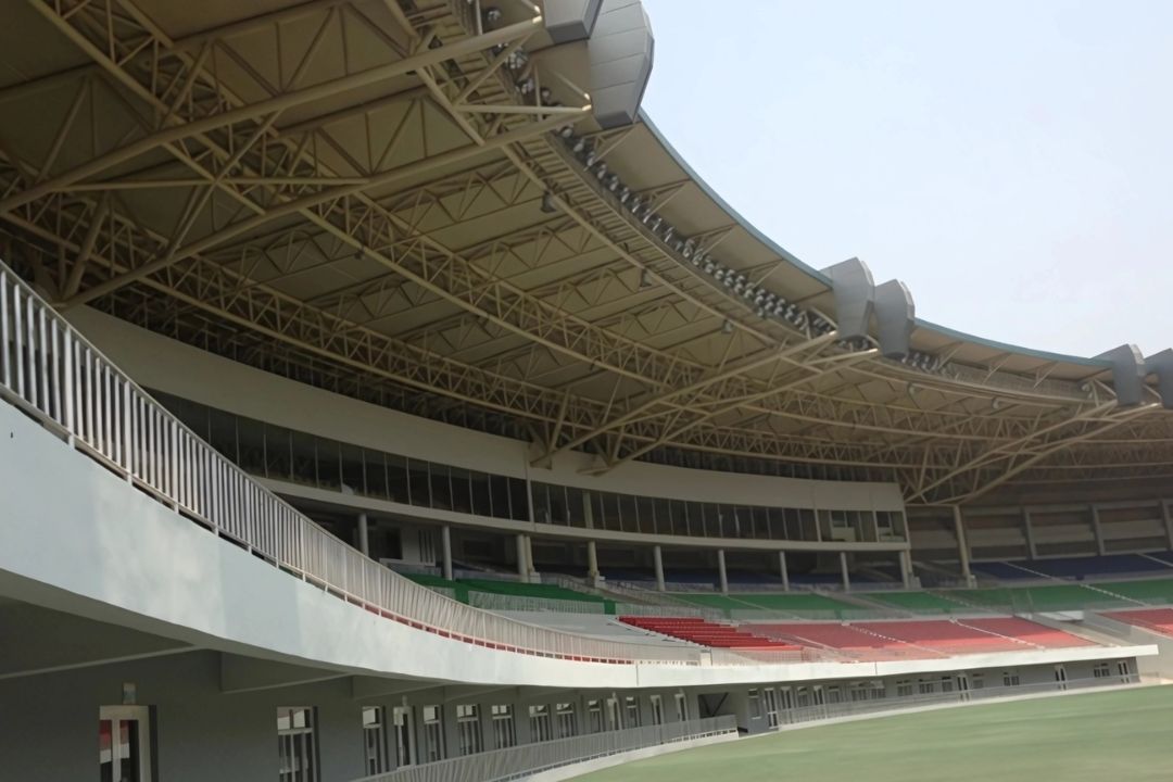 An interior photo of the completed 2013 Southeast Asian Games stadium in Myanmar, showing a close-up of the red, blue, and green seating, a section of the track, and a large scoreboard screen mounted on the far wall.