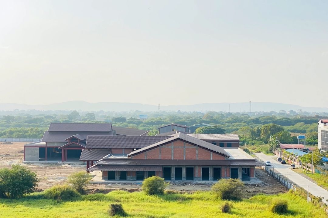 A photo of the Mandalay Jade Market project by Myanmar Yi Jin, showing the traditional style roofs on the main buildings and the exposed red steel framework of a separate structure in the background.