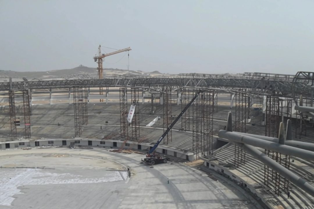 An elevated photo of the 2013 SEA Games stadium in Myanmar during the steel structure installation by Myanmar Yi Jin, showing the curved stadium bowl, a smaller crane on the field, and a larger crane in the background.