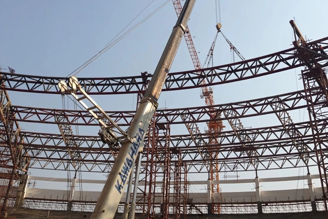 A close-up photo from inside the 2013 Southeast Asian Games stadium in Myanmar, focusing on the intricate steel structure being erected by Myanmar Yi Jin, with a large white crane prominently featured.