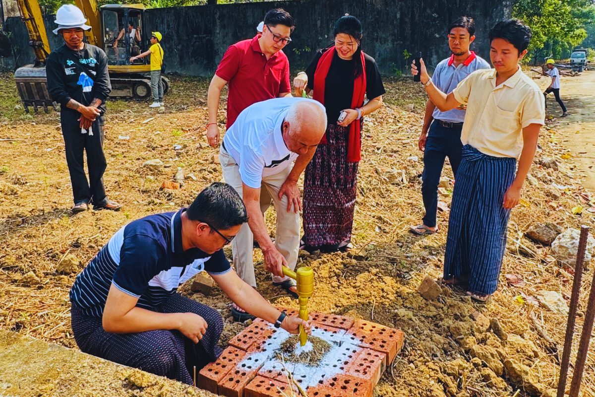 Executives and construction partners from Myanmar Yi Jin perform the ceremonial laying of bricks and gold-colored stakes at the groundbreaking site of a new car showroom and workshop building.