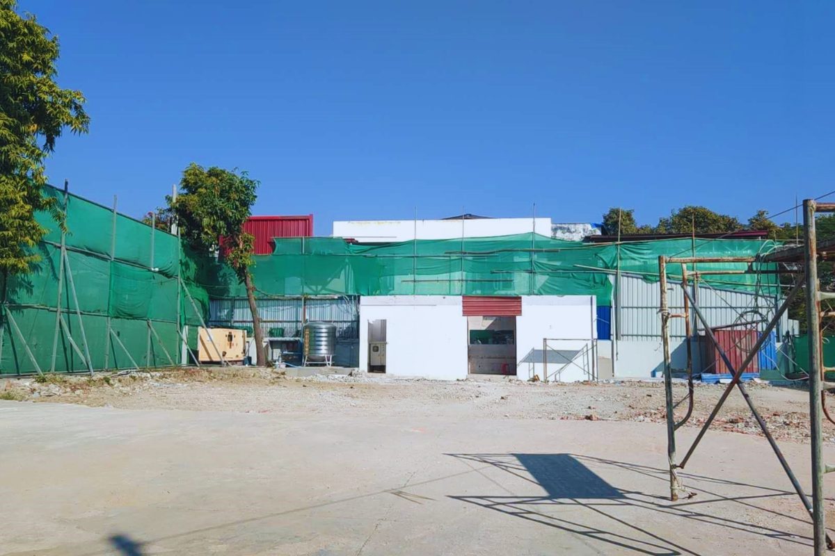 Exterior view of the Aung Kan Bo Trading Company Limited car showroom construction site in Mandalay, featuring a white building base with green safety netting and scaffolding by Myanmar Yi Jin.
