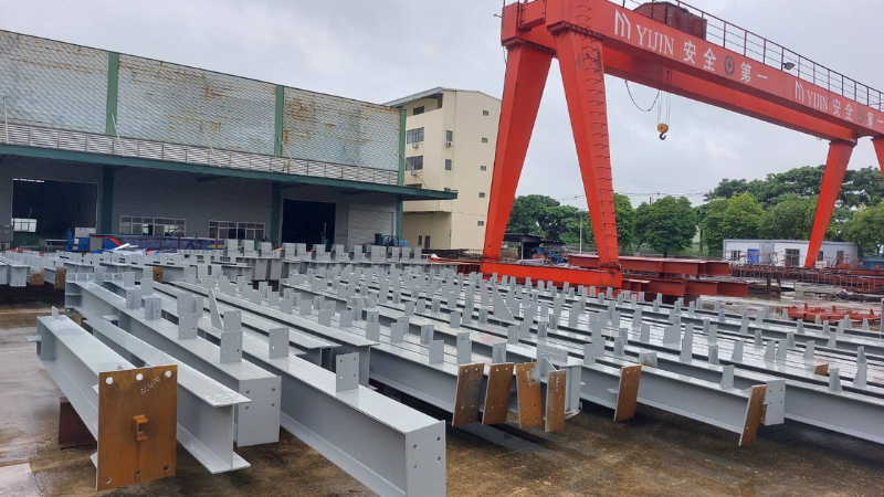 Precision-fabricated steel columns and roof trusses positioned under gantry cranes at Myanmar Yi Jin factory storage area before transport to Mandalay.