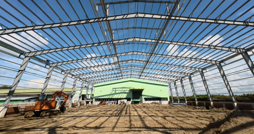 Wide-span steel roof truss erection and ground preparation inside the 60m x 36m x 9m warehouse extension for PAI Co. Ltd.